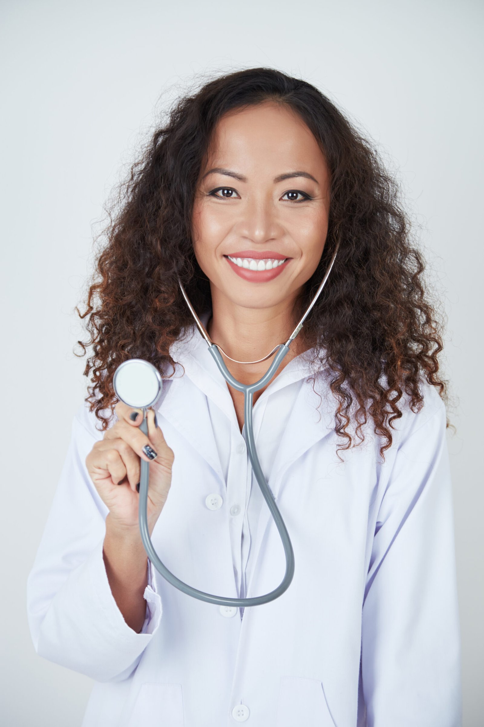 Portrait of young female doctor with curly hair holding stethoscope in front of the camera and smiling